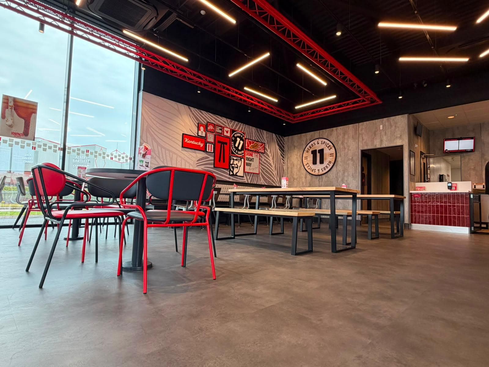 KFC dining room with red steel trusses, linear lights, timber bench tables and red and black chairs