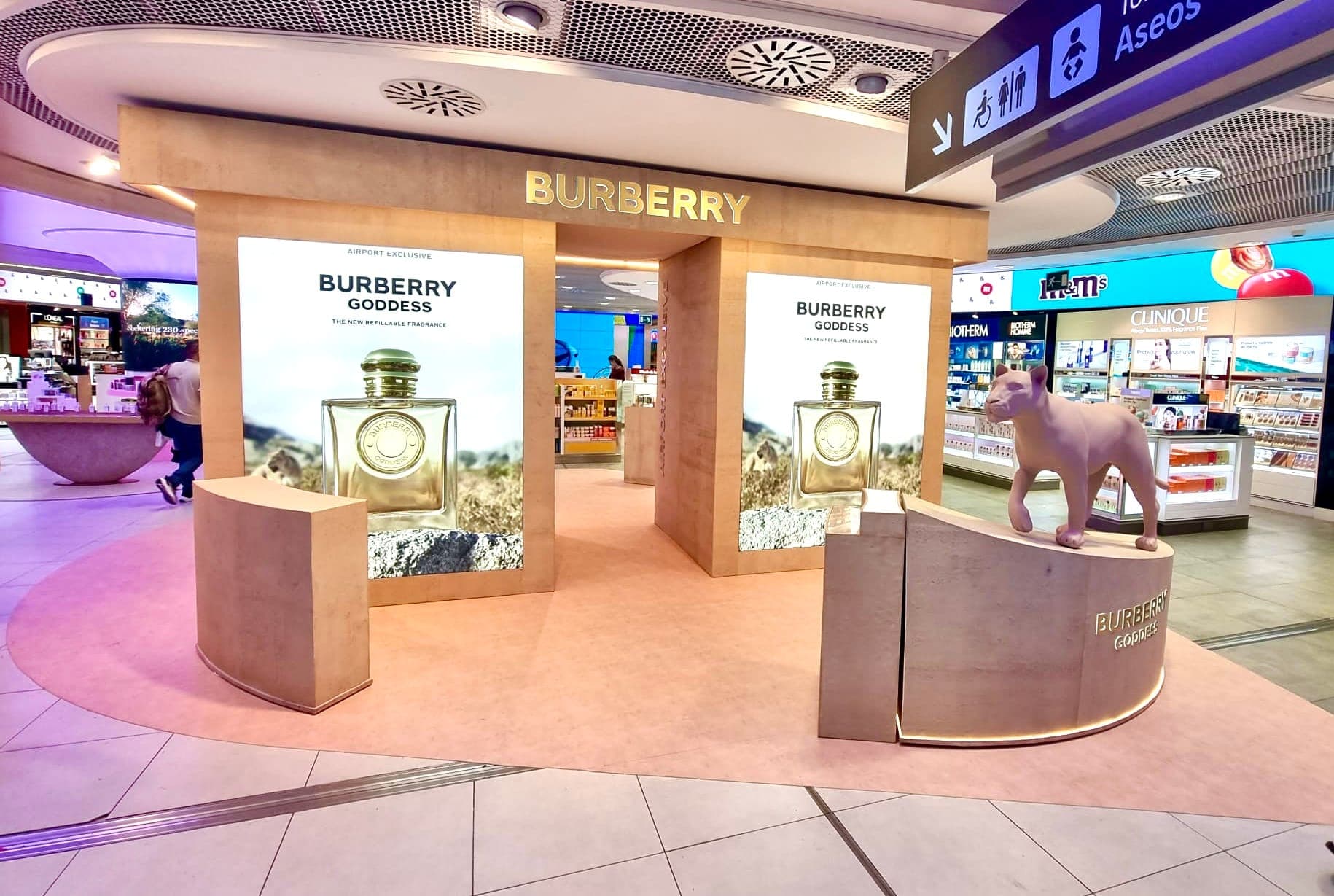 Burberry Goddess stand in an airport duty-free hall: pink stone-clad counters and plinths under a lit canopy