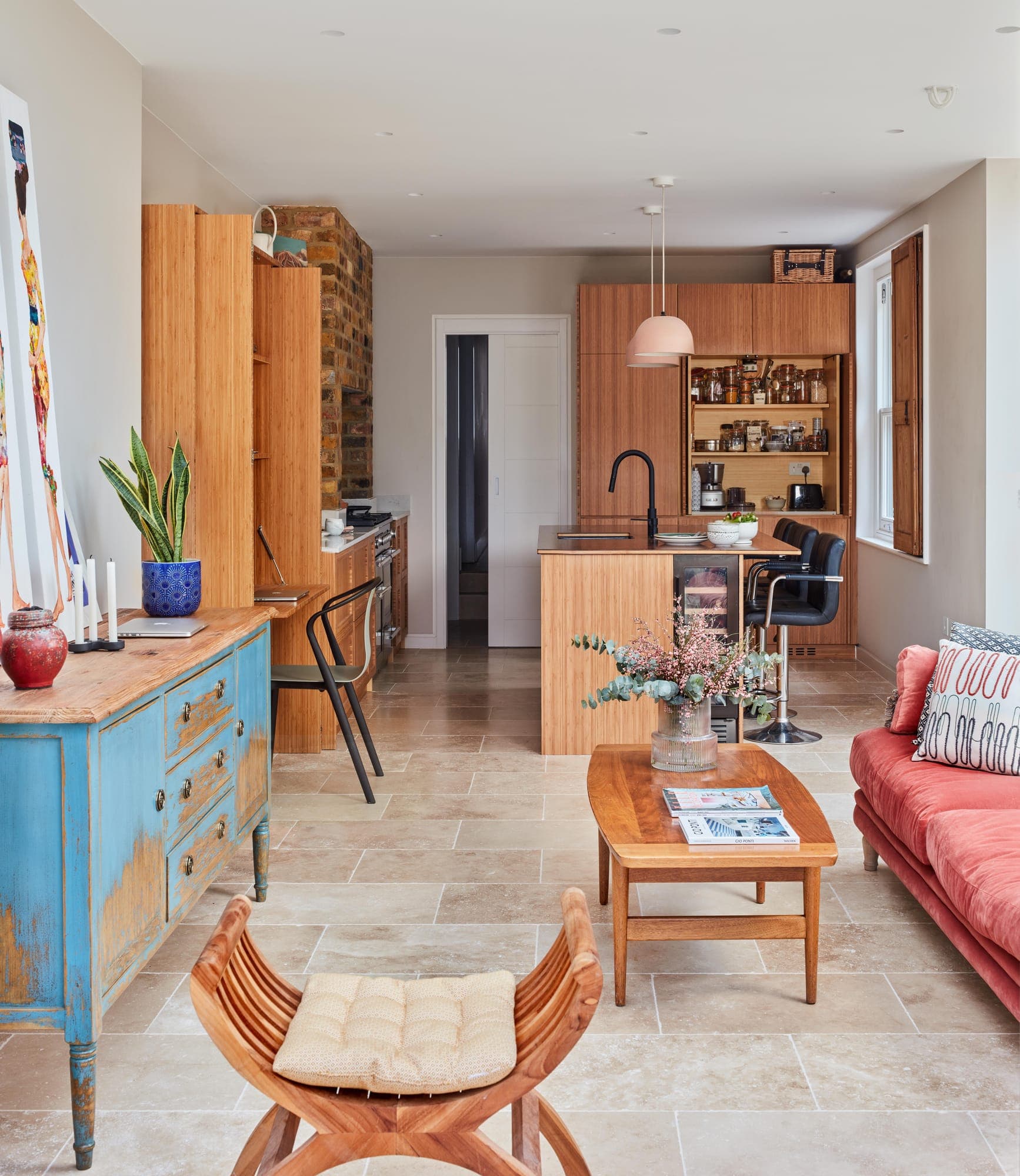 Open-plan living room leading to a bamboo kitchen, with a painted dresser and a red sofa in the foreground