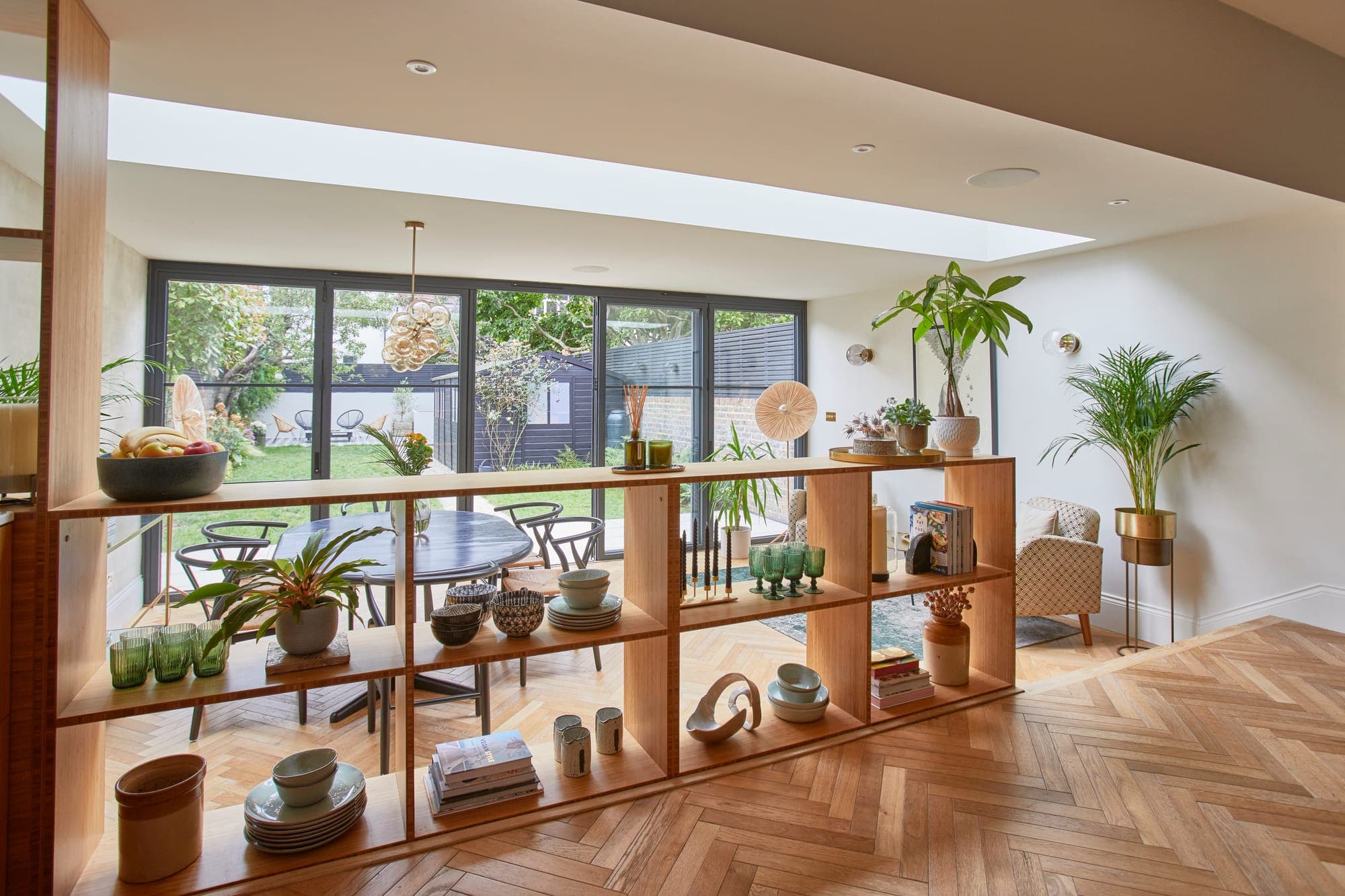 Open bamboo shelving dividing a kitchen from the dining area, full of plants and ceramics