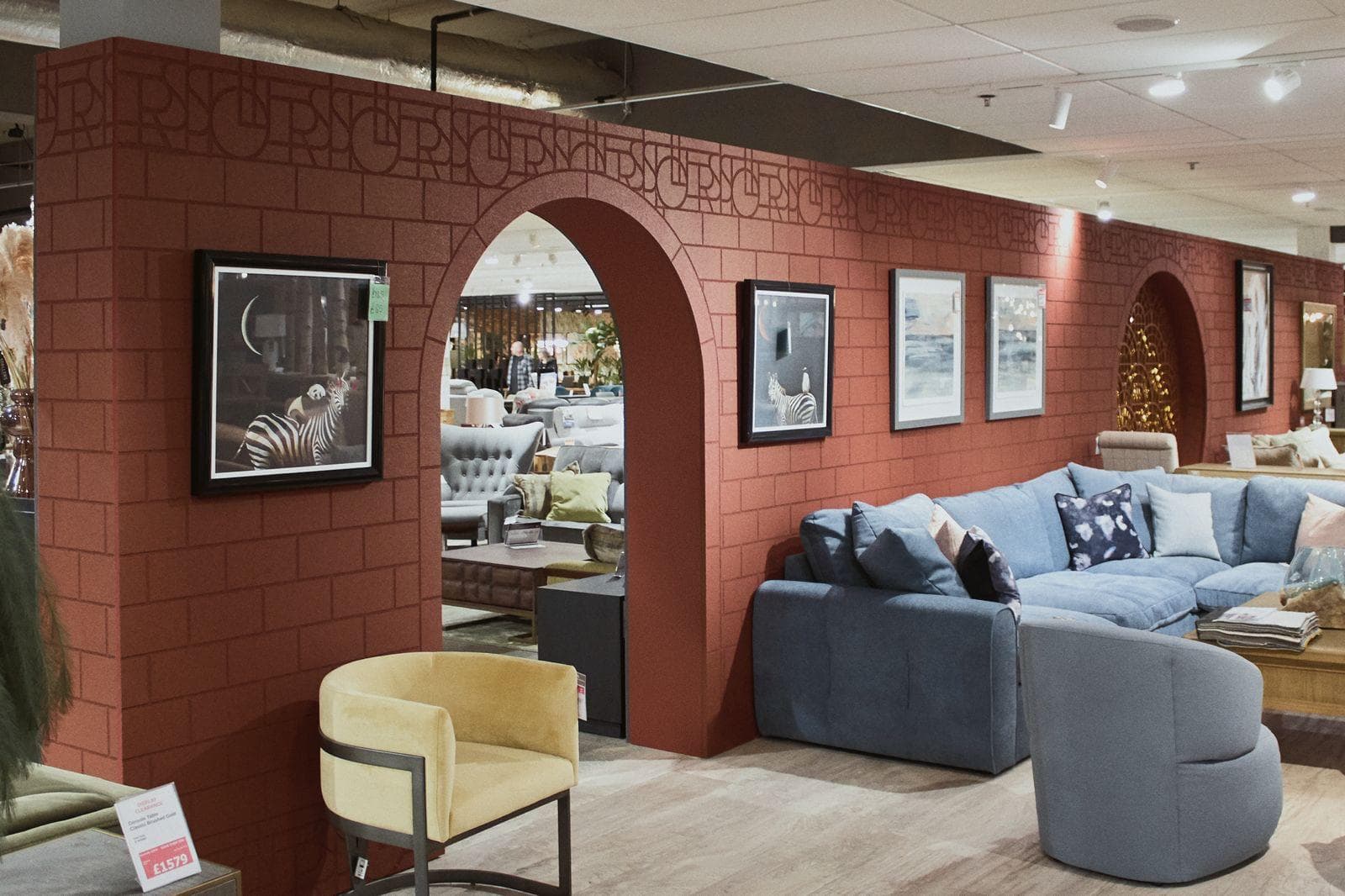Terracotta brick-pattern wall with an arched opening and a Stollers monogram frieze, framed pictures and sofas in front