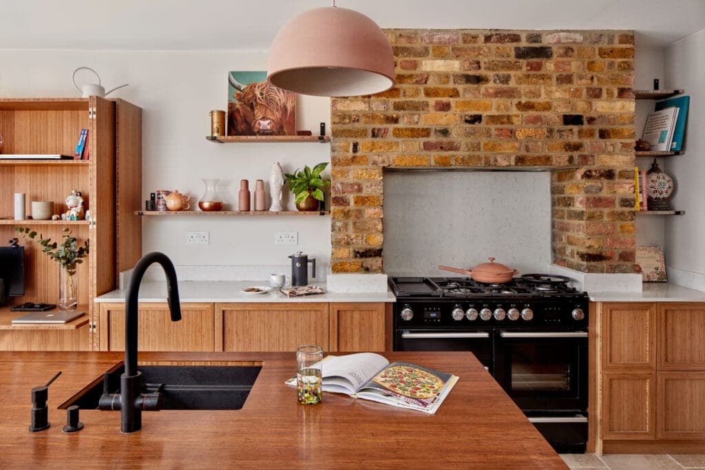 Bamboo kitchen units and open shelves around a brick chimney breast and range cooker