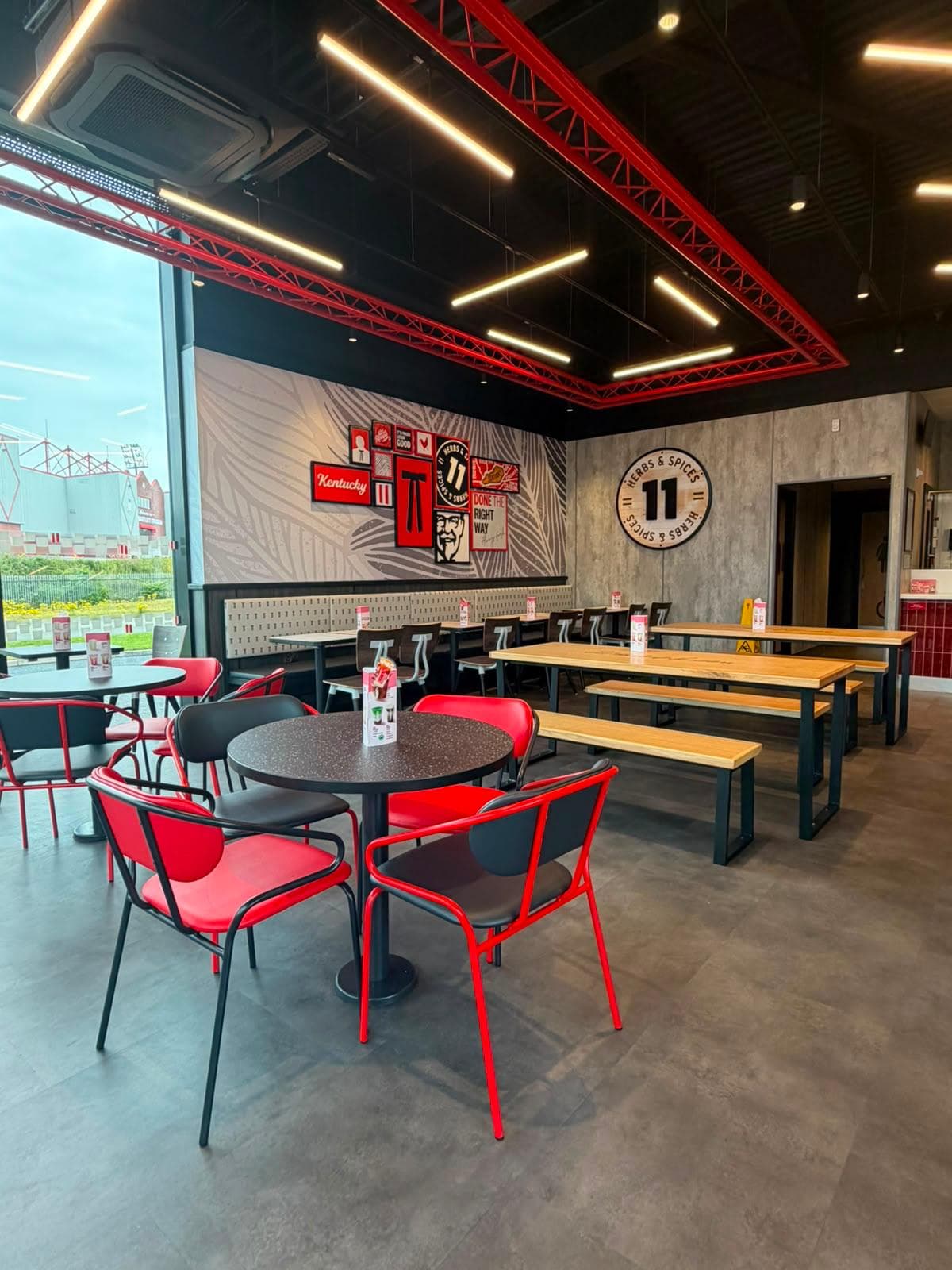Round tables with red and black chairs in front of timber bench tables and a KFC feature wall