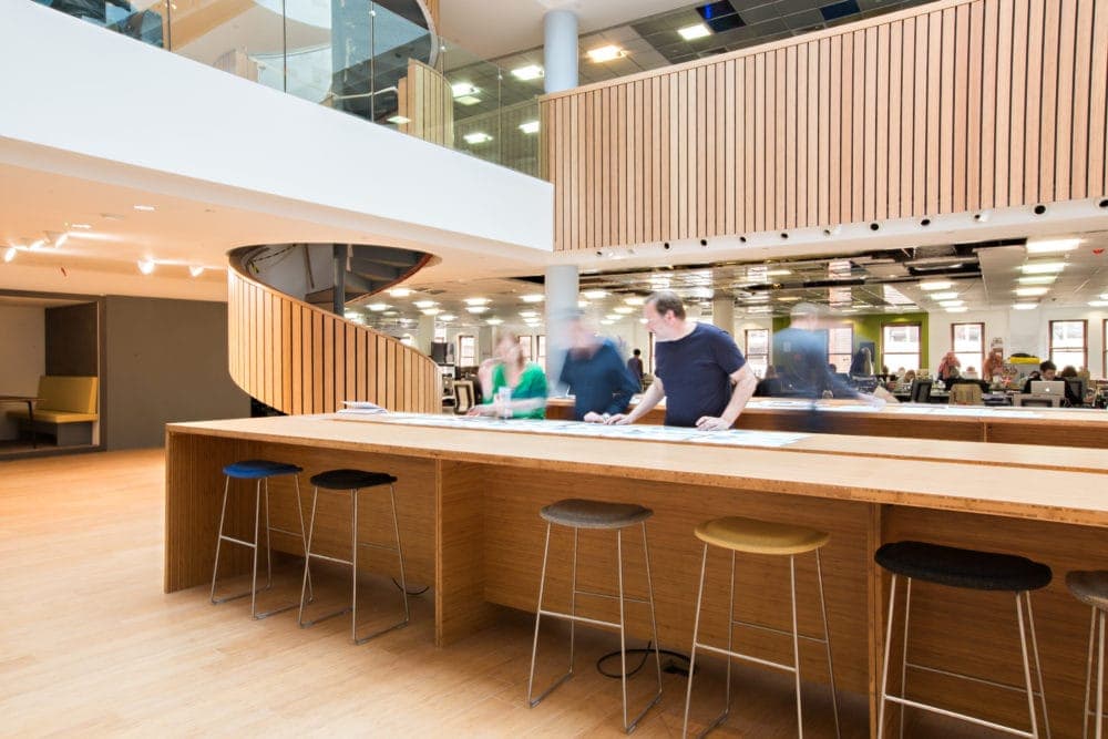 Open studio floor with a long bamboo bar counter and stools under a slatted gallery
