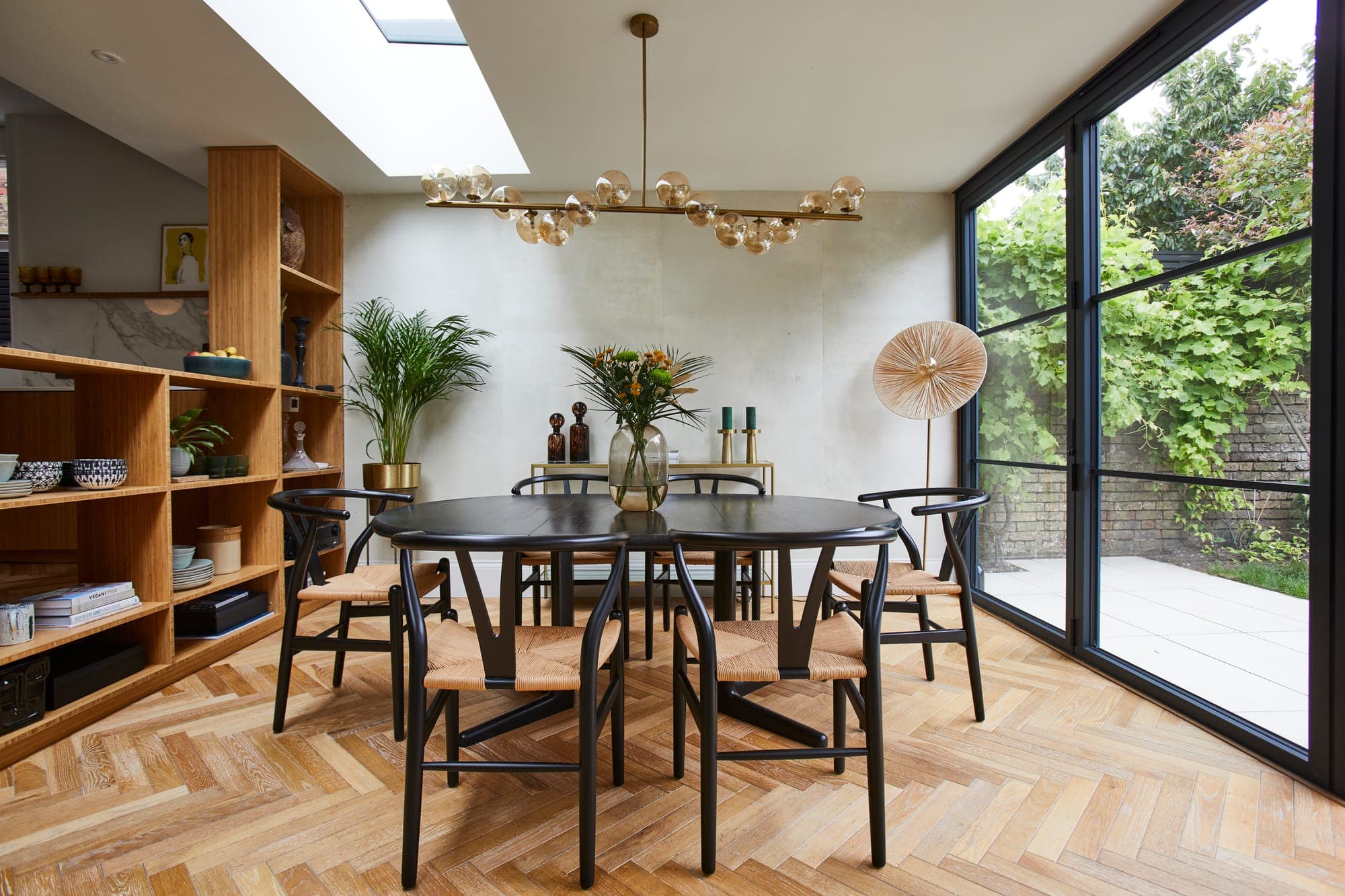 Dining area beside a wall of bamboo shelving, with a glazed extension looking onto the garden