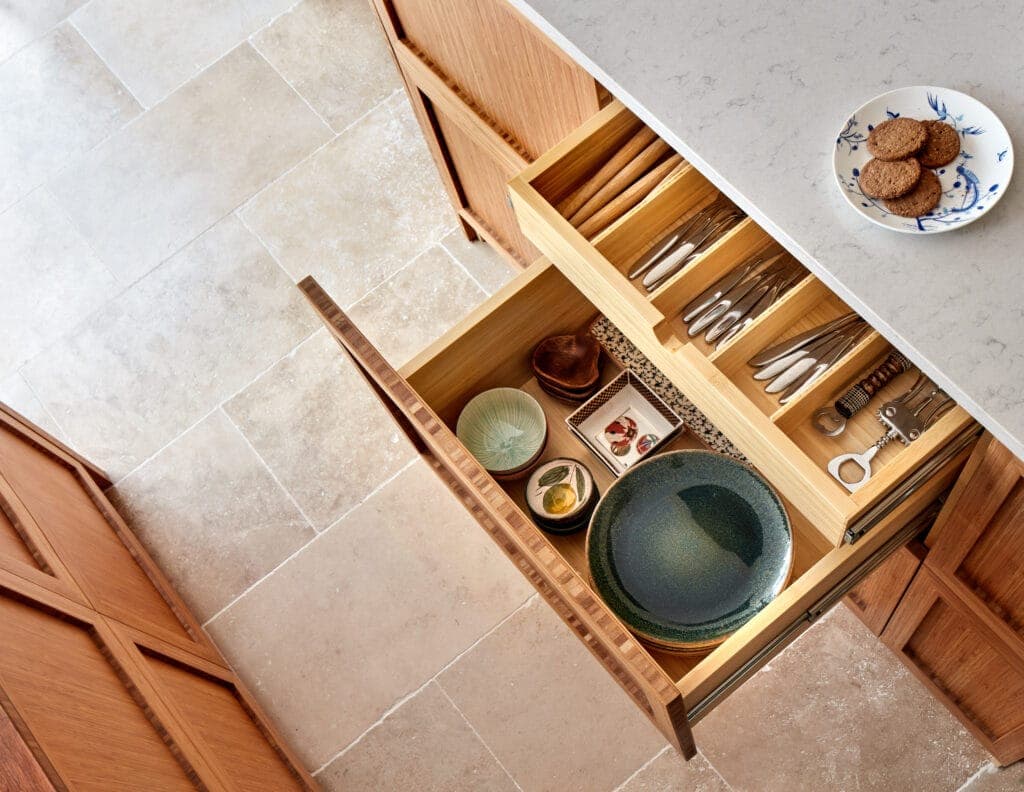 An open bamboo drawer with fitted dividers, seen from above against a stone floor
