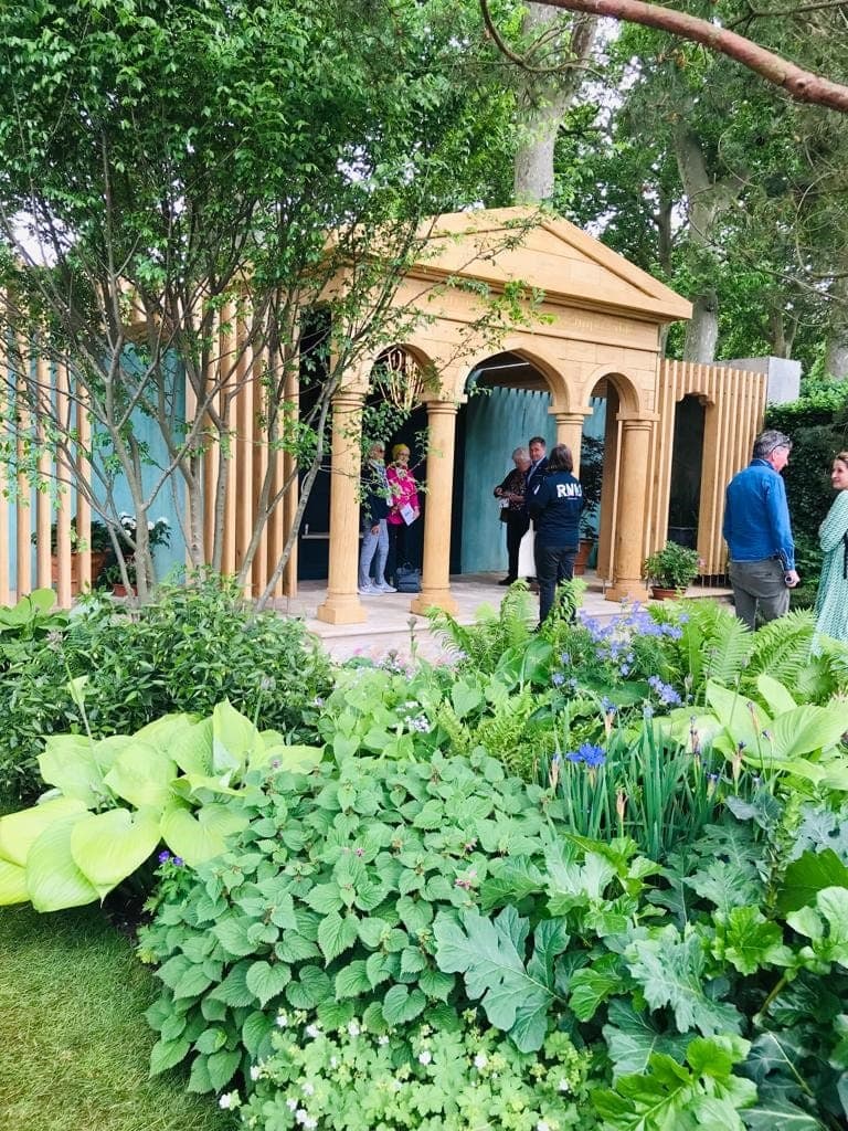 Lush green planting in front of a columned pavilion at the show garden
