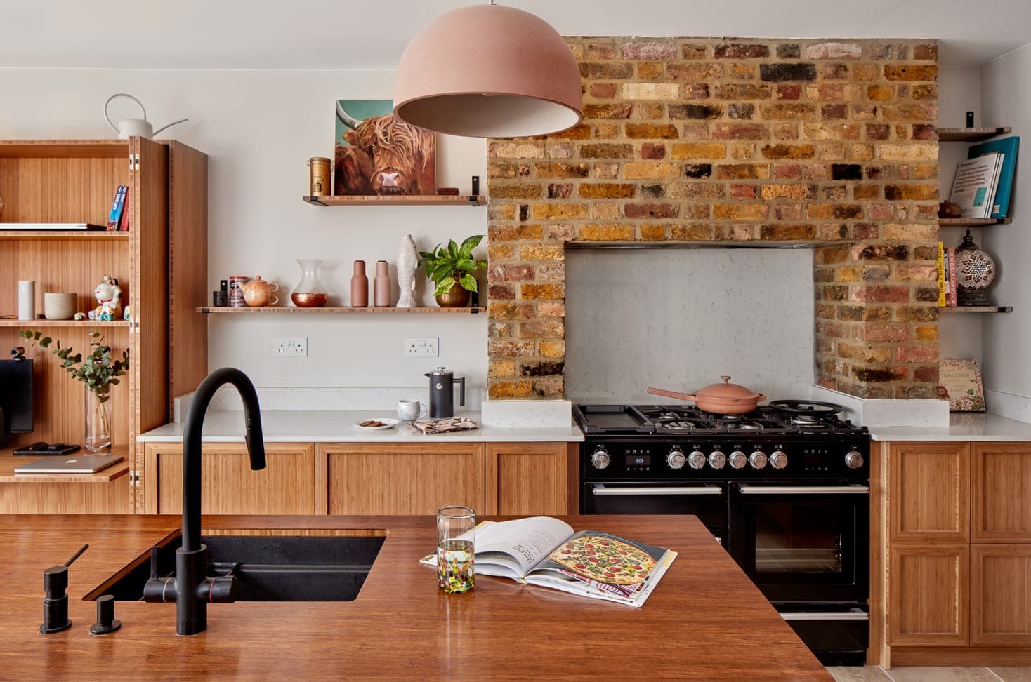 Kitchen with bamboo cabinetry and worktop beside an exposed brick chimney breast