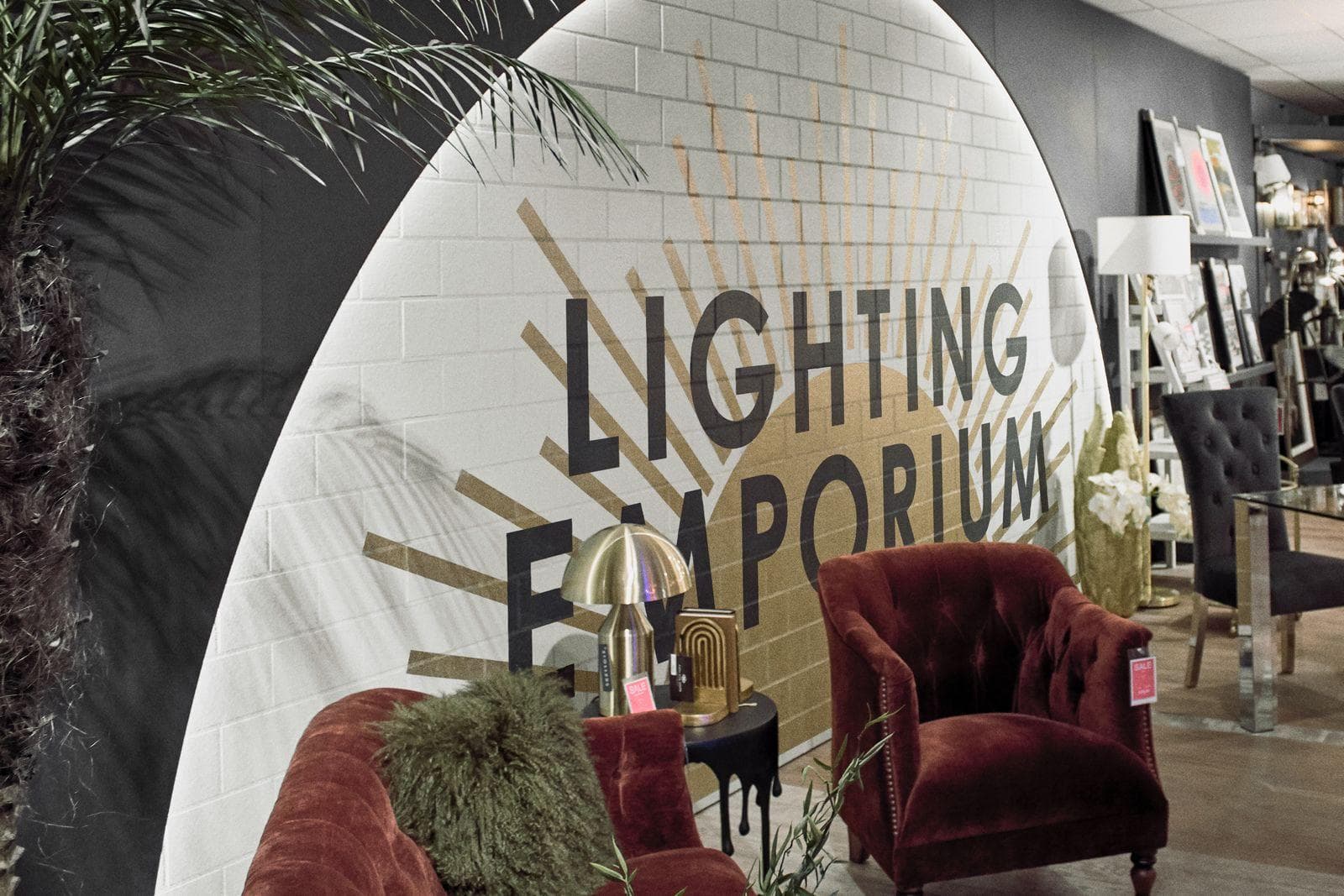 Backlit white arch with the Lighting Emporium sign behind red velvet armchairs and a brass lamp