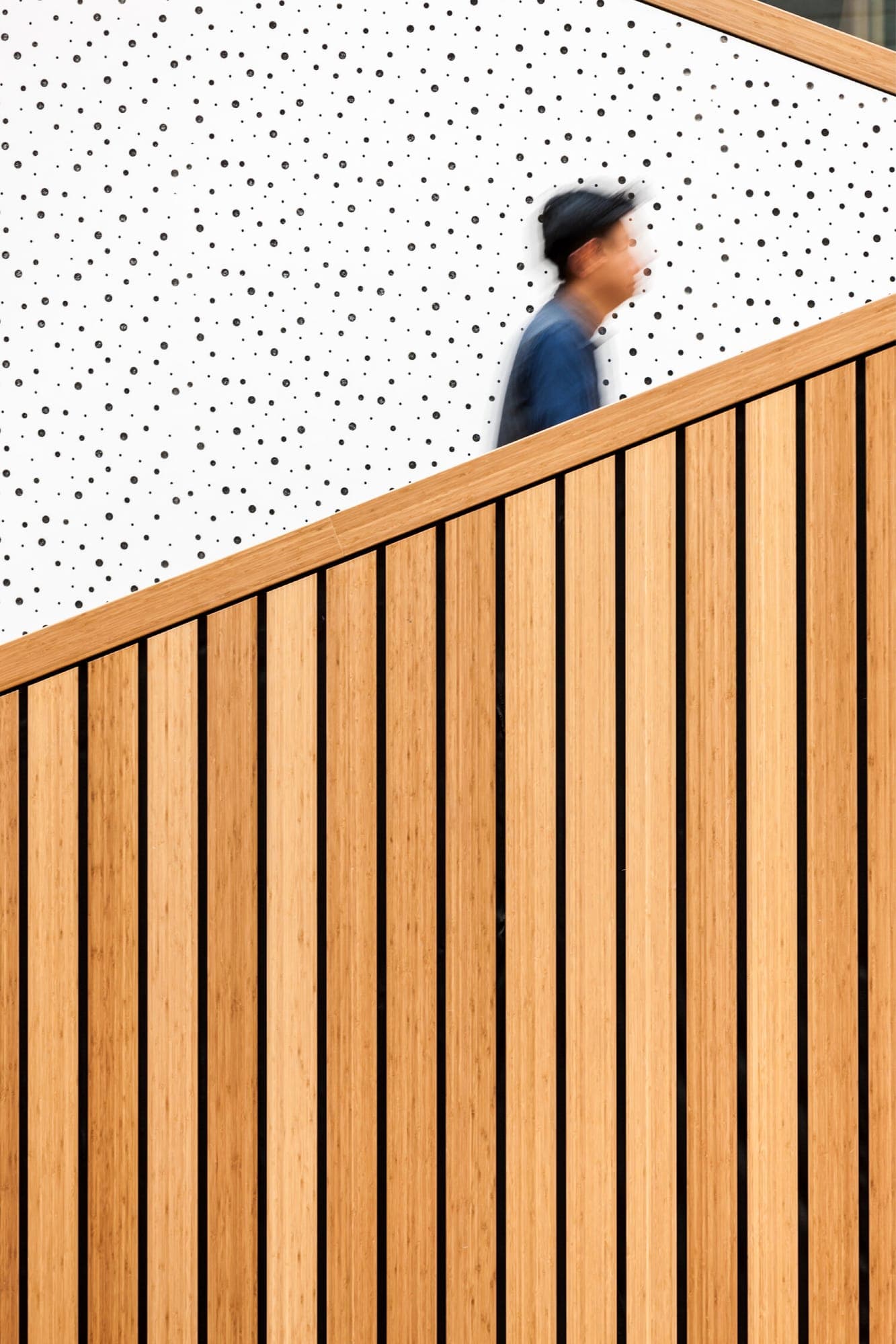 A figure climbing past a full-height balustrade of vertical bamboo slats