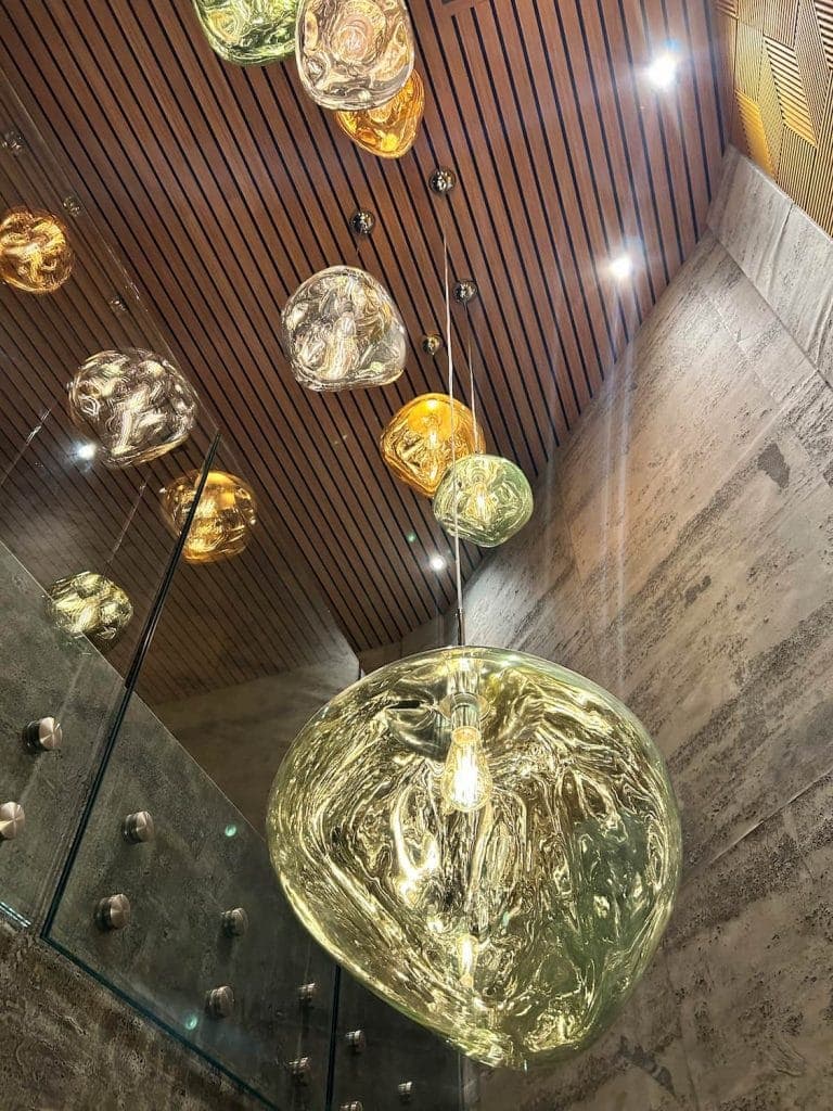 Looking up the stair void past glass pendant lights to a slatted timber ceiling