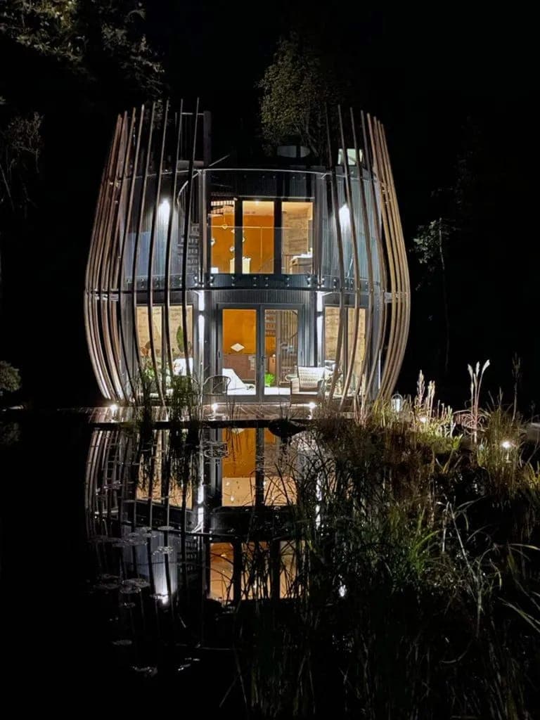 The Poppy lit from within at night, its slatted shell reflected in the water