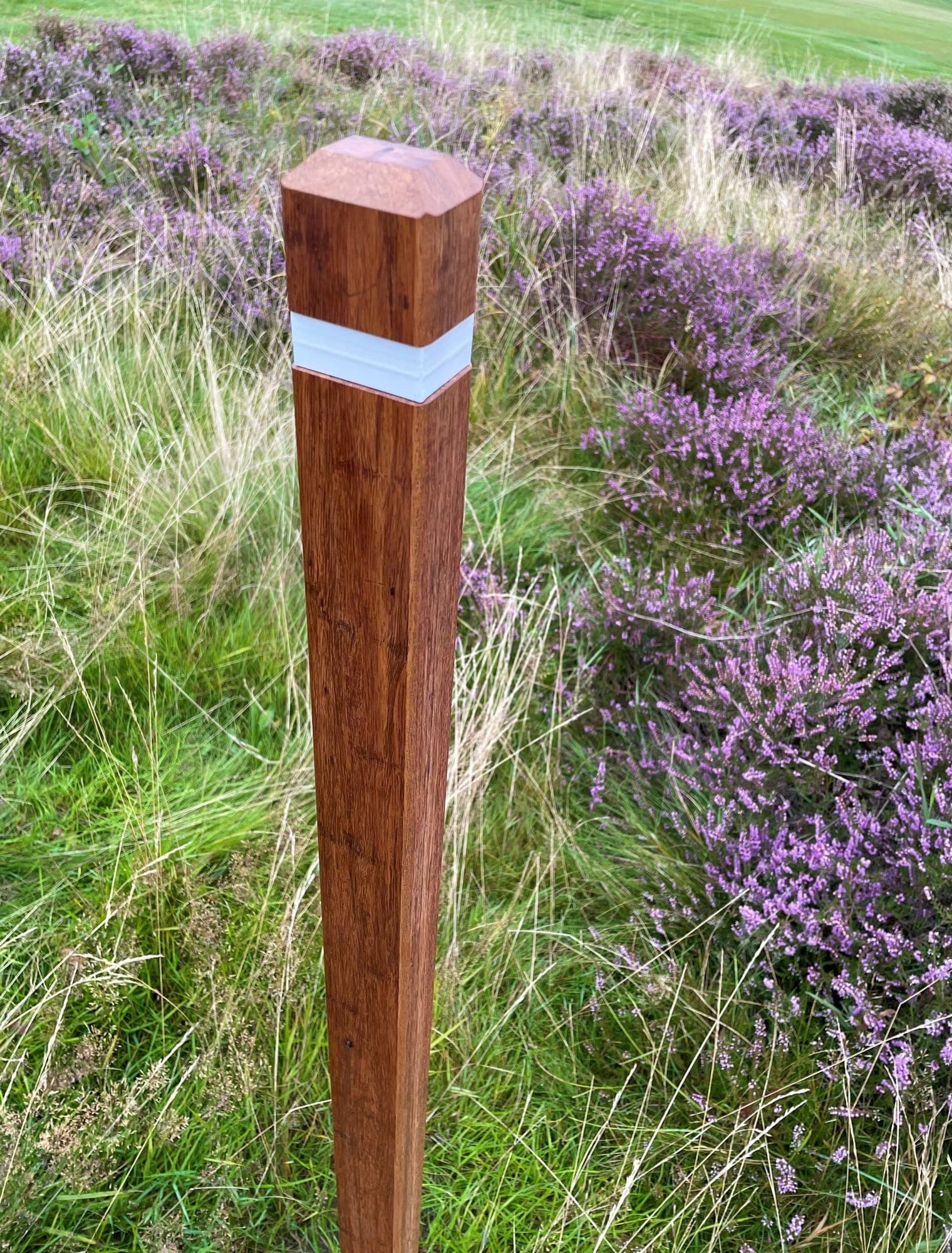 A square bamboo marker post with a white band, among grasses and heather