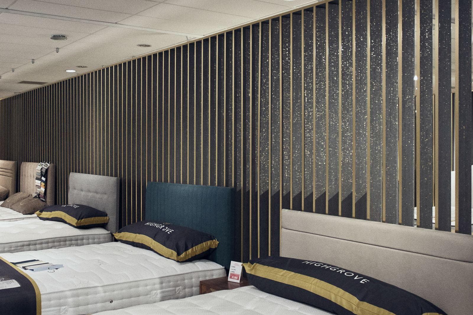 Beds lined up in front of a long wall of dark slats with brass strips between them