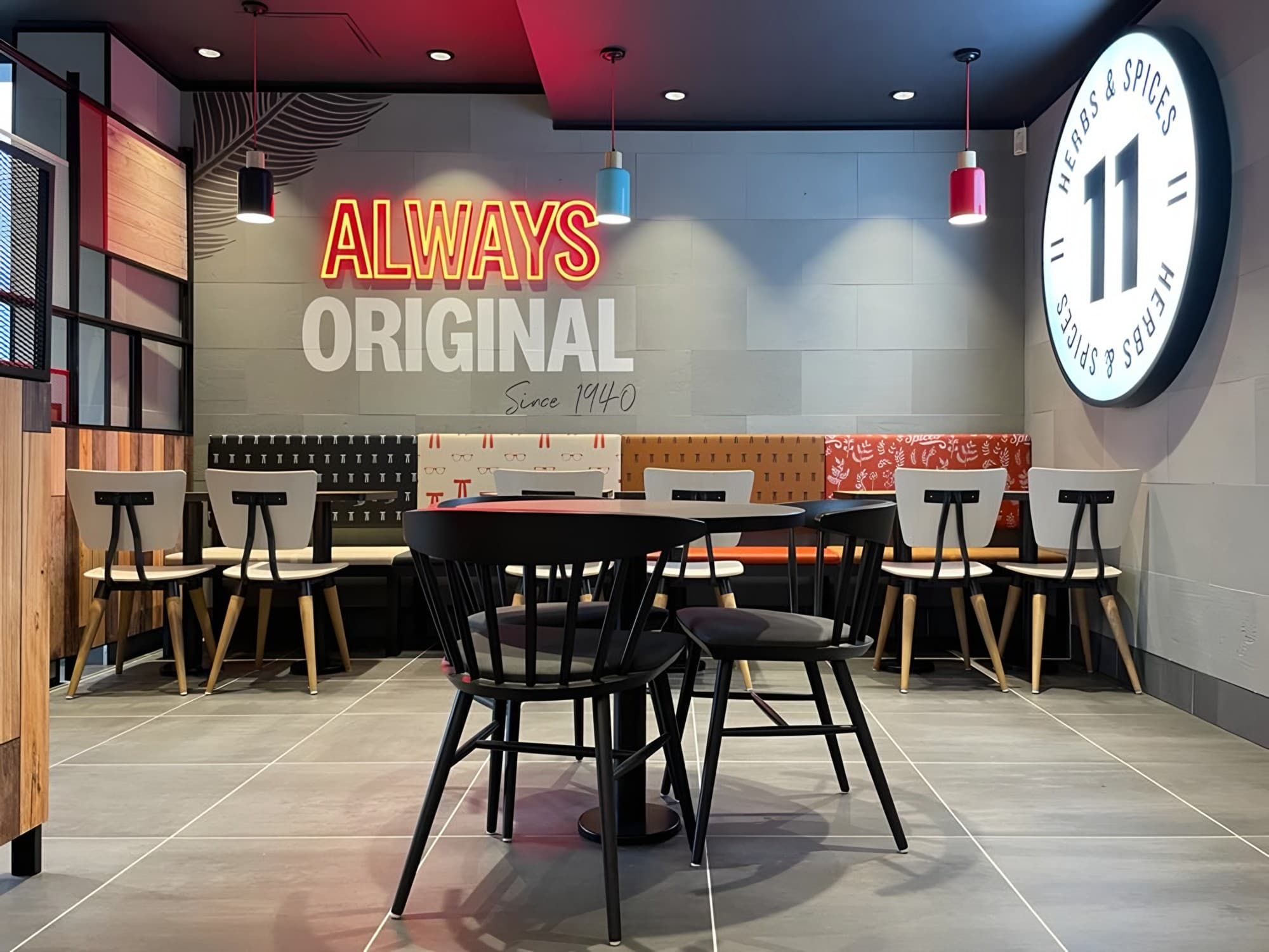 Patterned banquette seating beneath an 'Always Original' neon sign and an illuminated 11 Herbs & Spices roundel