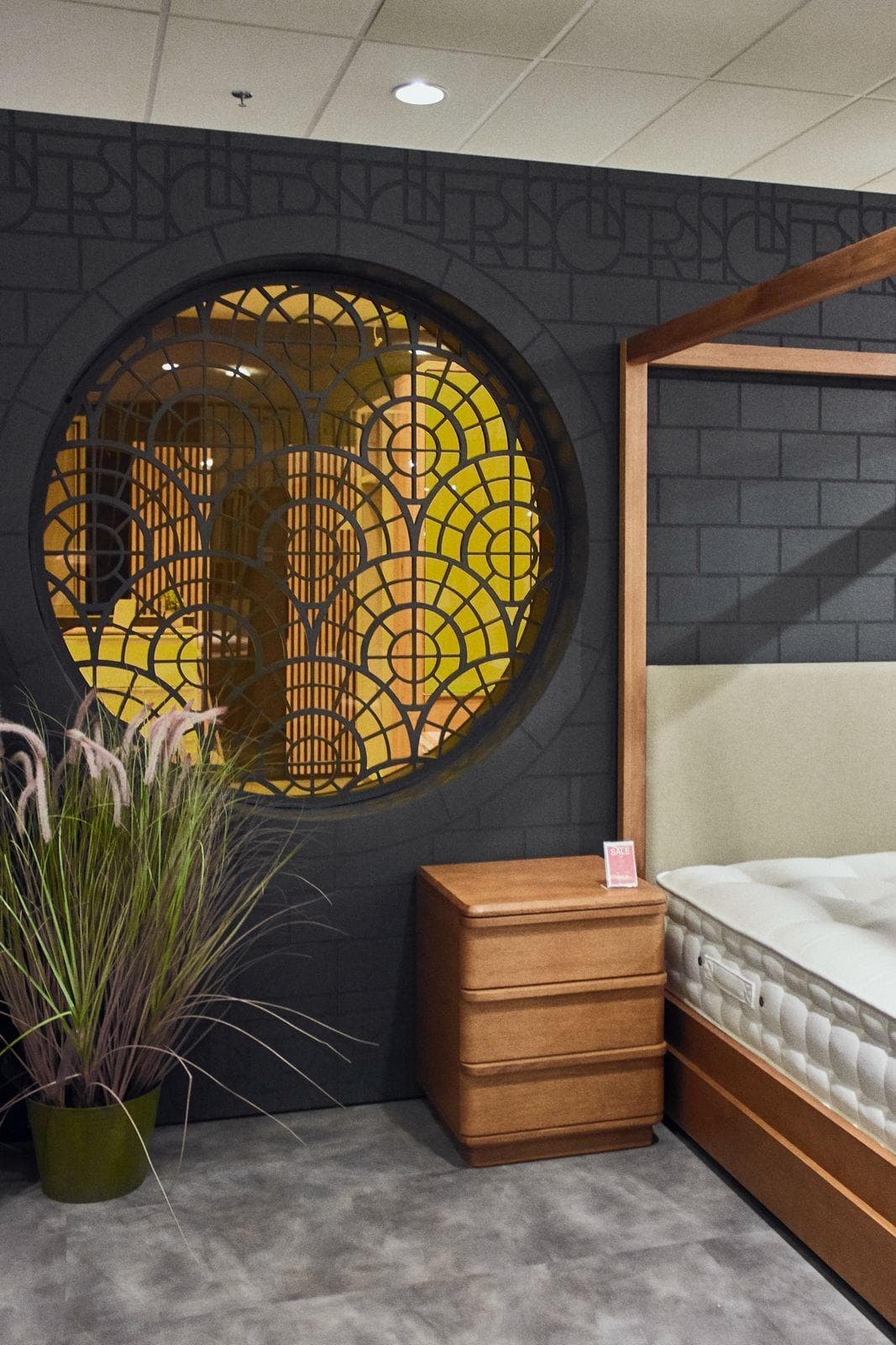 Round art deco screen set into a dark brick-pattern wall beside a four-poster bed