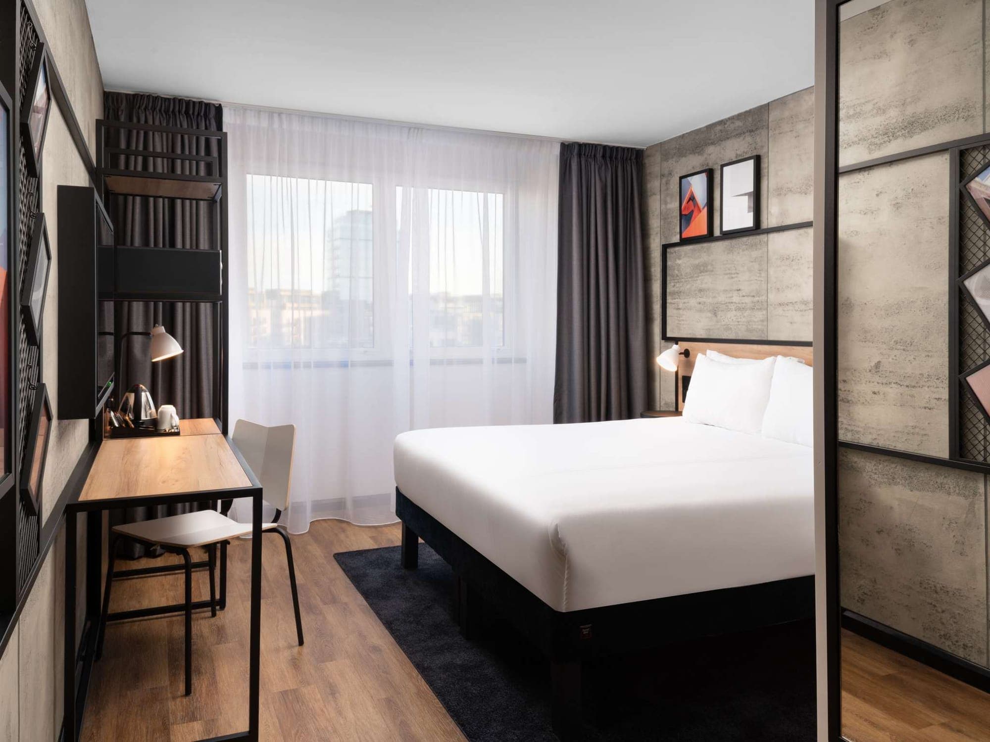 Hotel bedroom with a grey stone-effect clad wall behind the bed and a timber desk by the window